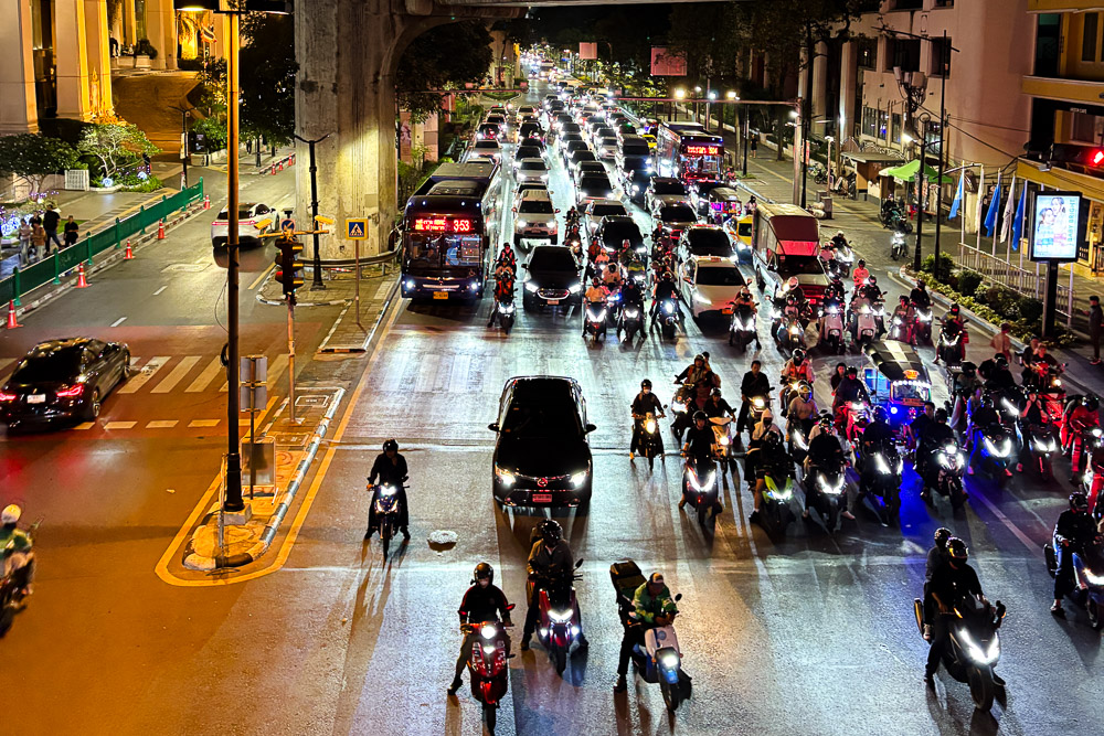 A traffic jam in bangkok early in the night. A long line of cars and motorcycle lining up with their headlights illuminating the road.