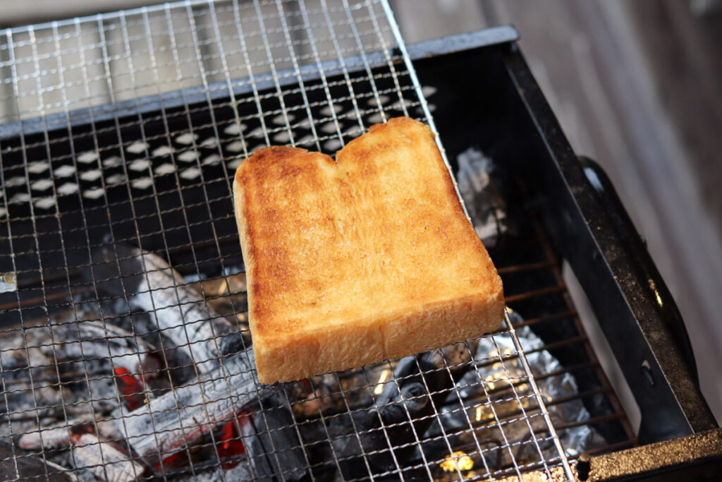 A golden brown, perfectly cooked, Shokupan over a fire on the grill at a camp site in Japan.