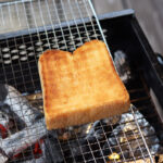 A golden brown, perfectly cooked, Shokupan over a fire grill at a camp site.