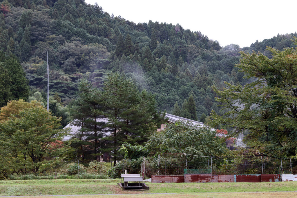 A camping ground in Toyooka, Japan, showing a field with a mountain behind full or trees.