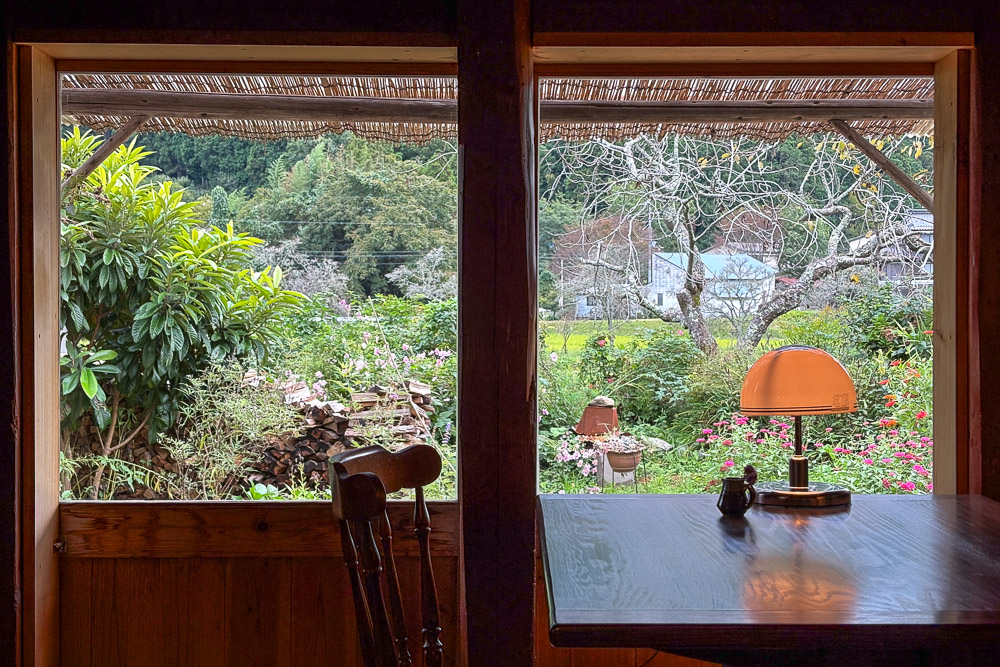 A peaceful cafe setting in Japan suburb with wooden decoration and big windeows to a garden view from 居七十七（いなとな）.​