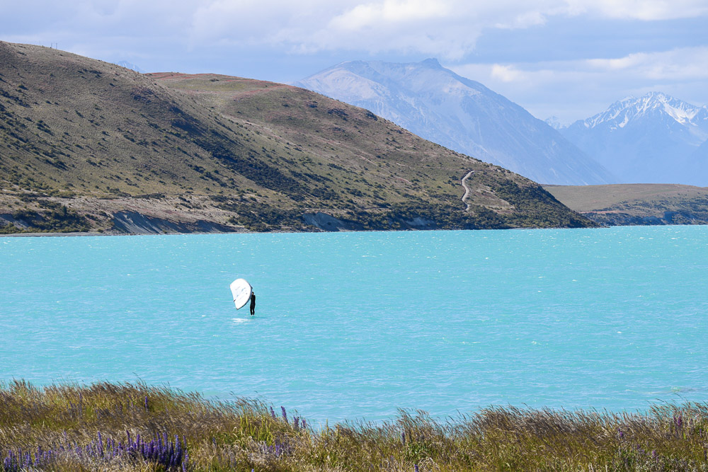 Summer in Lake tekapo with a person surfing on the bright blue water