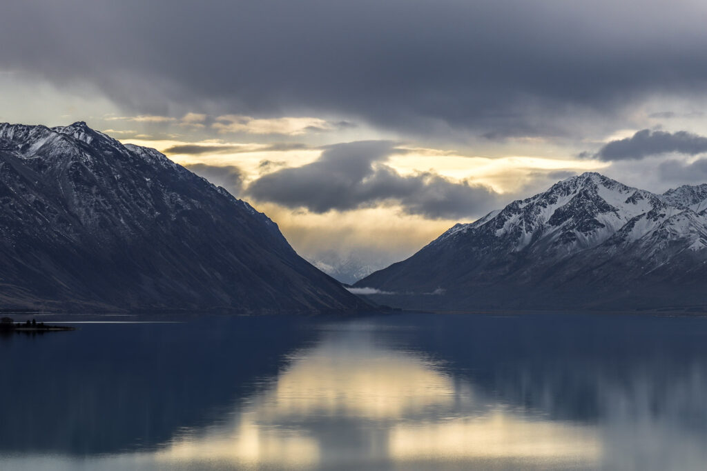 The sun setting visible through the gap between two mountains with snow on the peak, taken in autumn at Kake Tekapo.