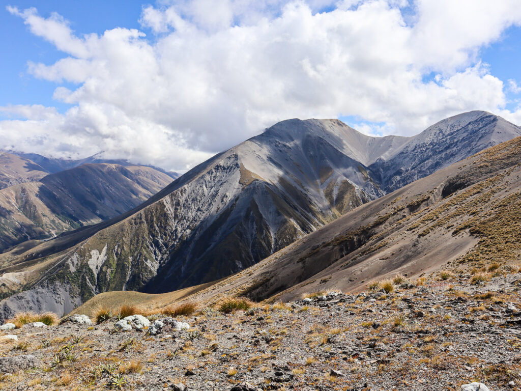 A more rocky mountain surface only covered partially by brown weeds, a cloud casting a shadow on its side giving out a dramatic scene.