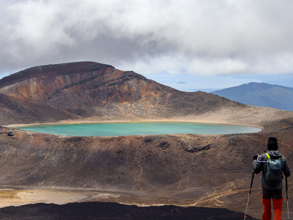 The Blue Lake on Togariro Alpine Crossing. The view during a cloudy day as a hiker hiked by the blue lake in full view from the peak.