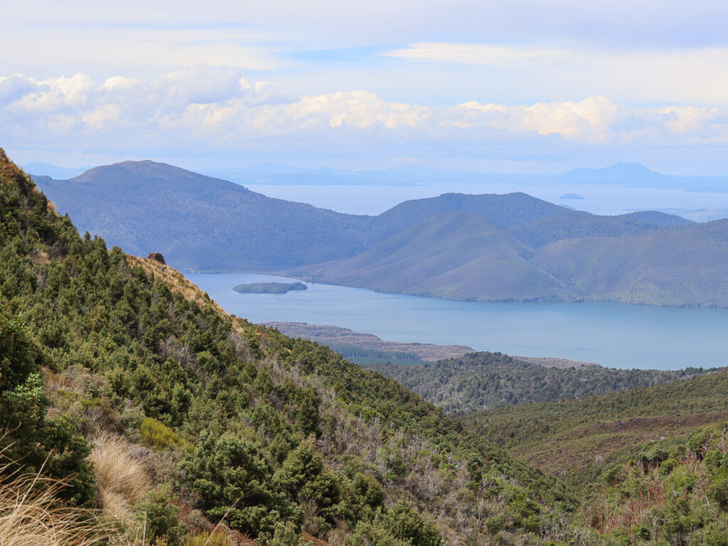 A view towards the end of Ketetahi descent on togariro alpine crossing in summer. A view from the side of the mountain with a lake visible further away.