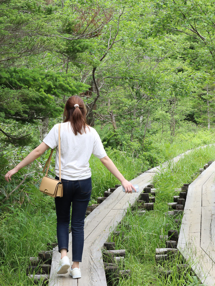 A girl playfully walking on the woodplank pathway at a hiking spot in Kamikochi.