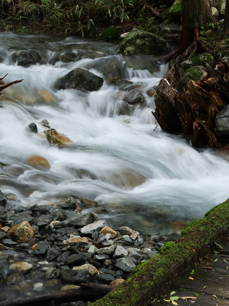 Dekasawa stream flowing under a small bridge covered with moss, taken with a low shutter speed. The relaxing sound of water during a hike in Kamikochi.