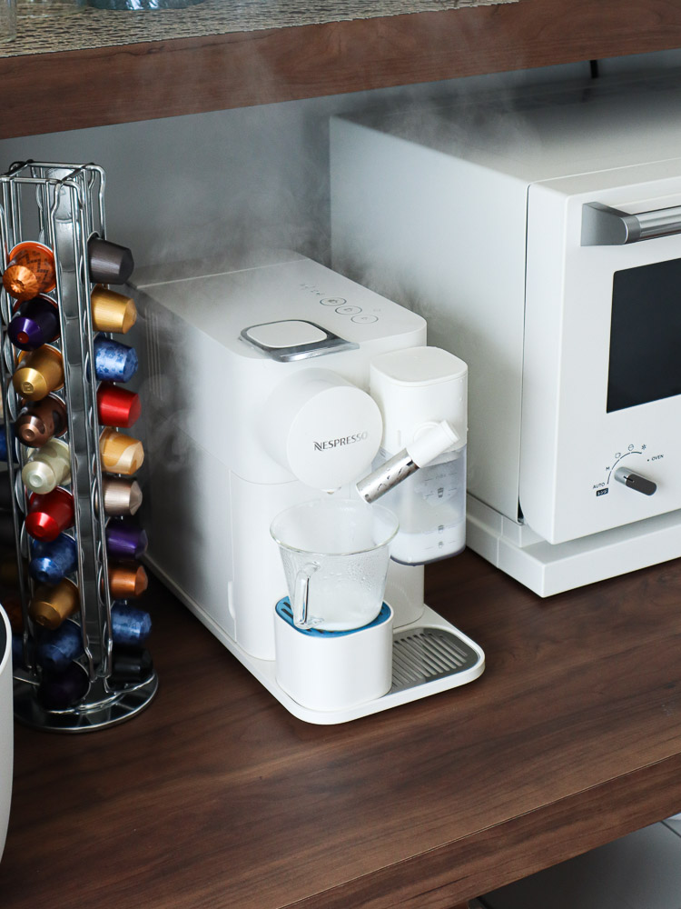 A white Nespresso machine as it is steaming, next to it is a white Balmuda The Range.