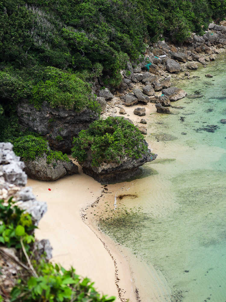 the beach of Ndakachina, in Okinawa, emerald colored water, white sandy beace and green covering the rocks.