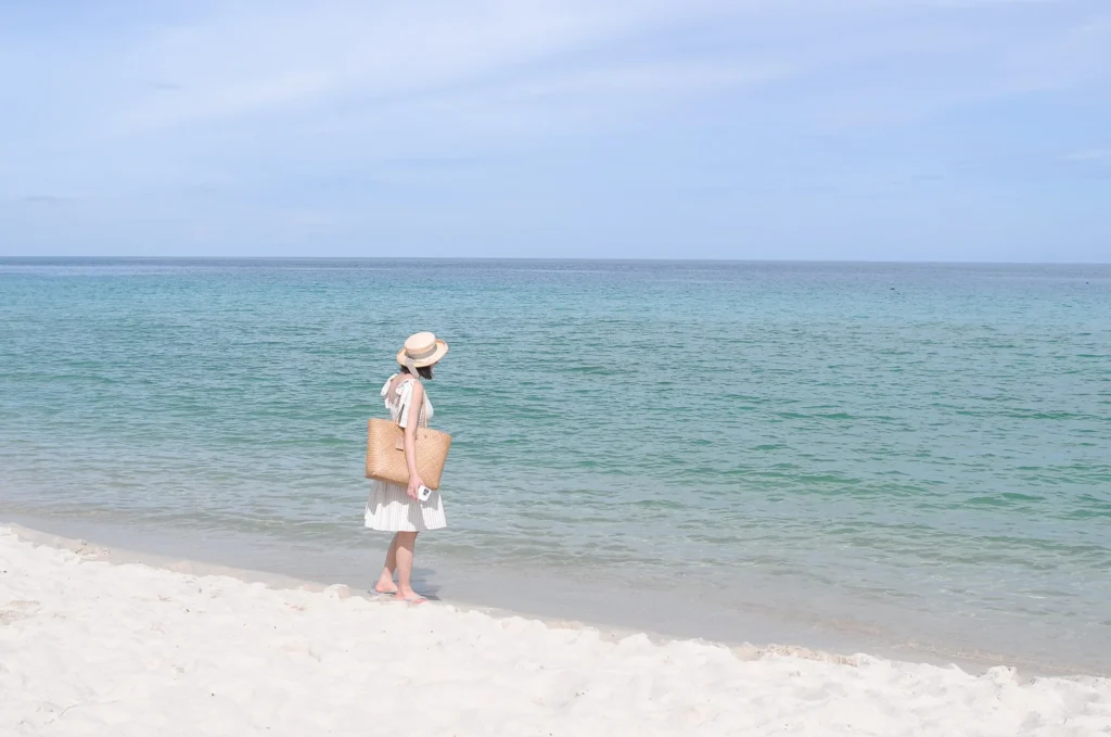 A white sandy beach on Samui Island and a girl in a white dress. The midday sun shines bright but not as bright as her.