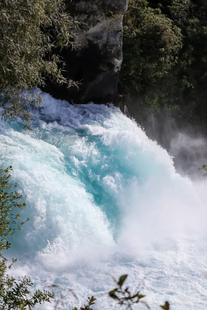 A magnificent crystal blue waterfall at Huka Falls, Taupō. A large and rapidly flowing water gushing off the edge.