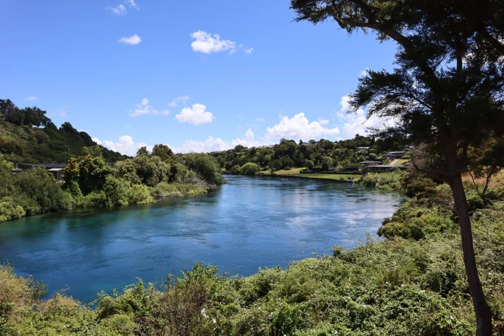 Waikato River, the section flowing through the residential area in Taupō town. Deep blue water surrounded by greeneries.