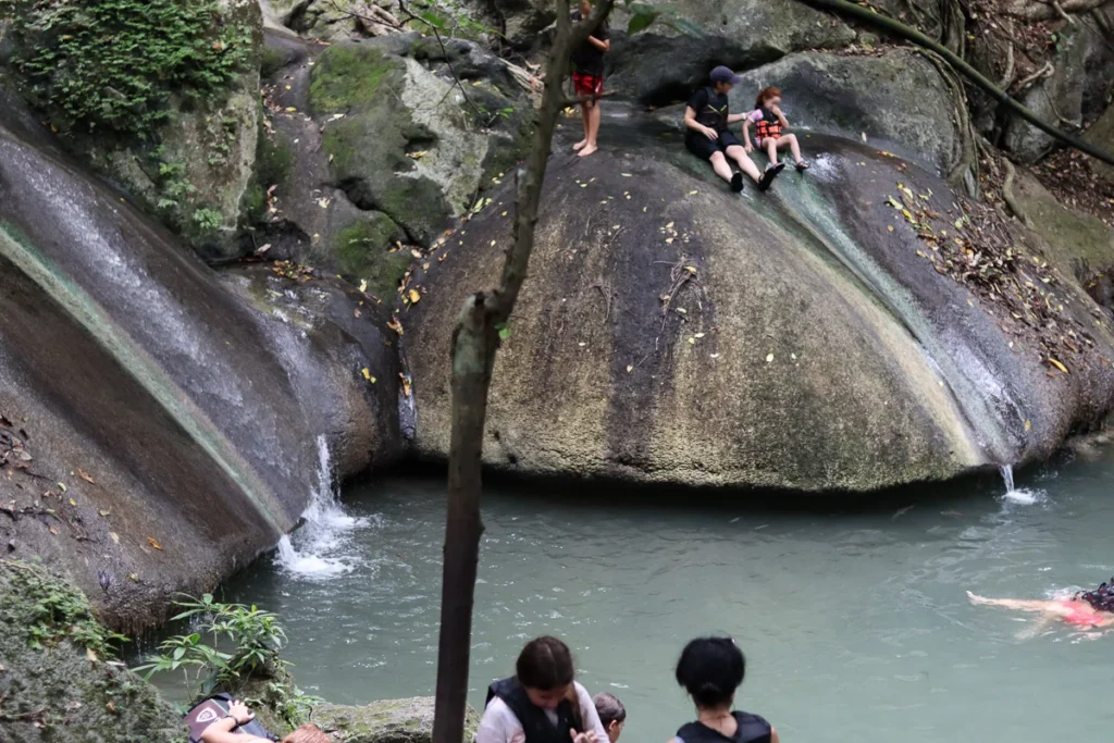 People enjoying their time and using the waterfall as a slider at Erawan 4th floor waterfall.